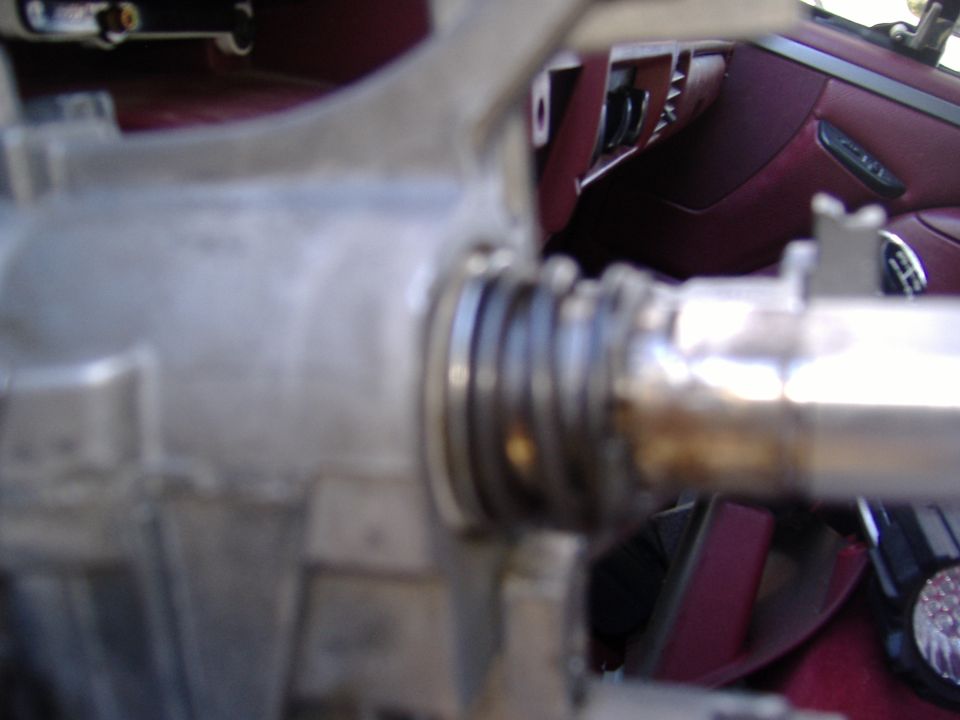 Close-up of a metal steering column component with visible springs and a maroon interior in the background