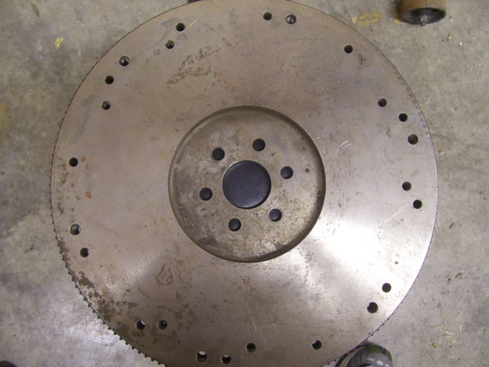 Metal flywheel with bolt holes and gear teeth, showing rust and wear