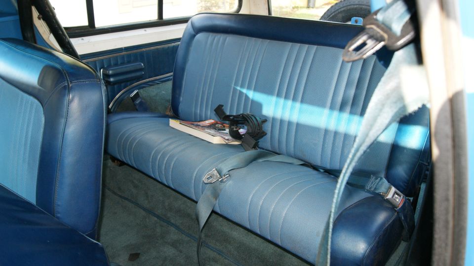 Blue vinyl rear bench seat with seat belts and green carpet inside an SUV