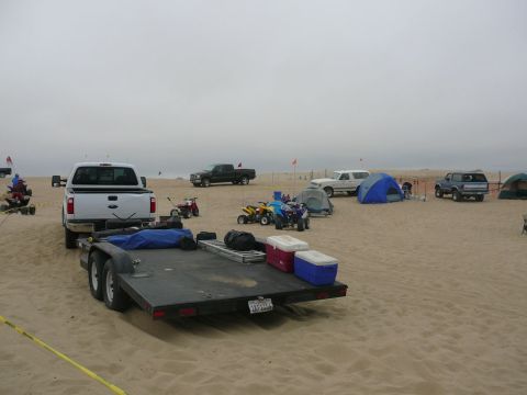 1988 Ford Bronco - A beach scene with multiple vehicles, tents, and ATVs suggests a recreational outing.
