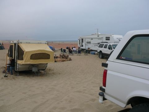 1988 Ford Bronco - A beach campsite scene with multiple RVs and a pop-up trailer set up on the sand.