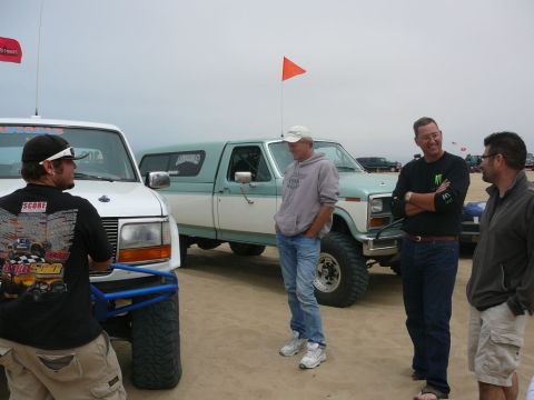 1988 Ford Bronco - A group of men stand around a classic two-tone Ford pickup truck with a camper shell, possibly at a desert or beach event.