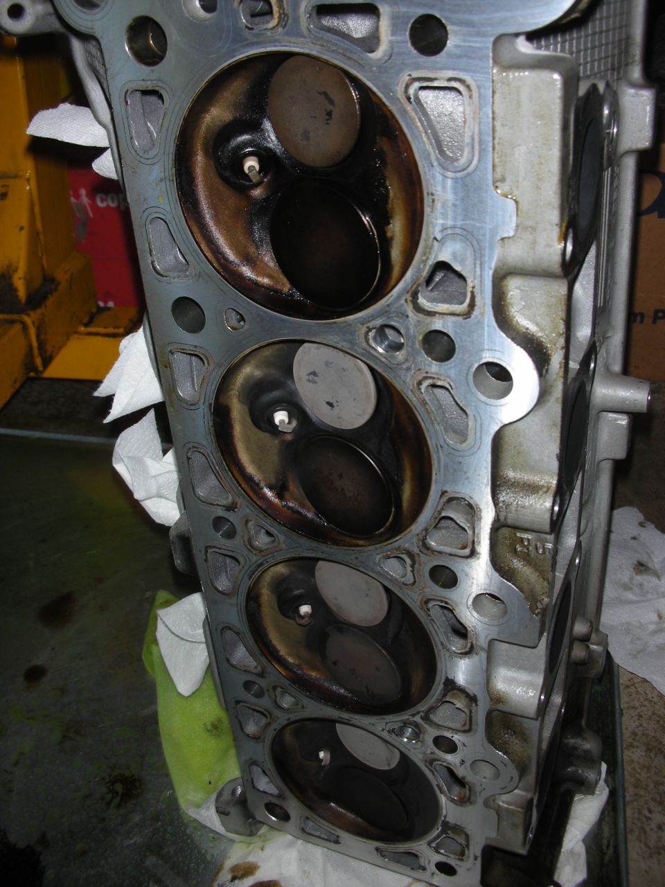 Engine cylinder head with four visible combustion chambers, showing valves and carbon buildup