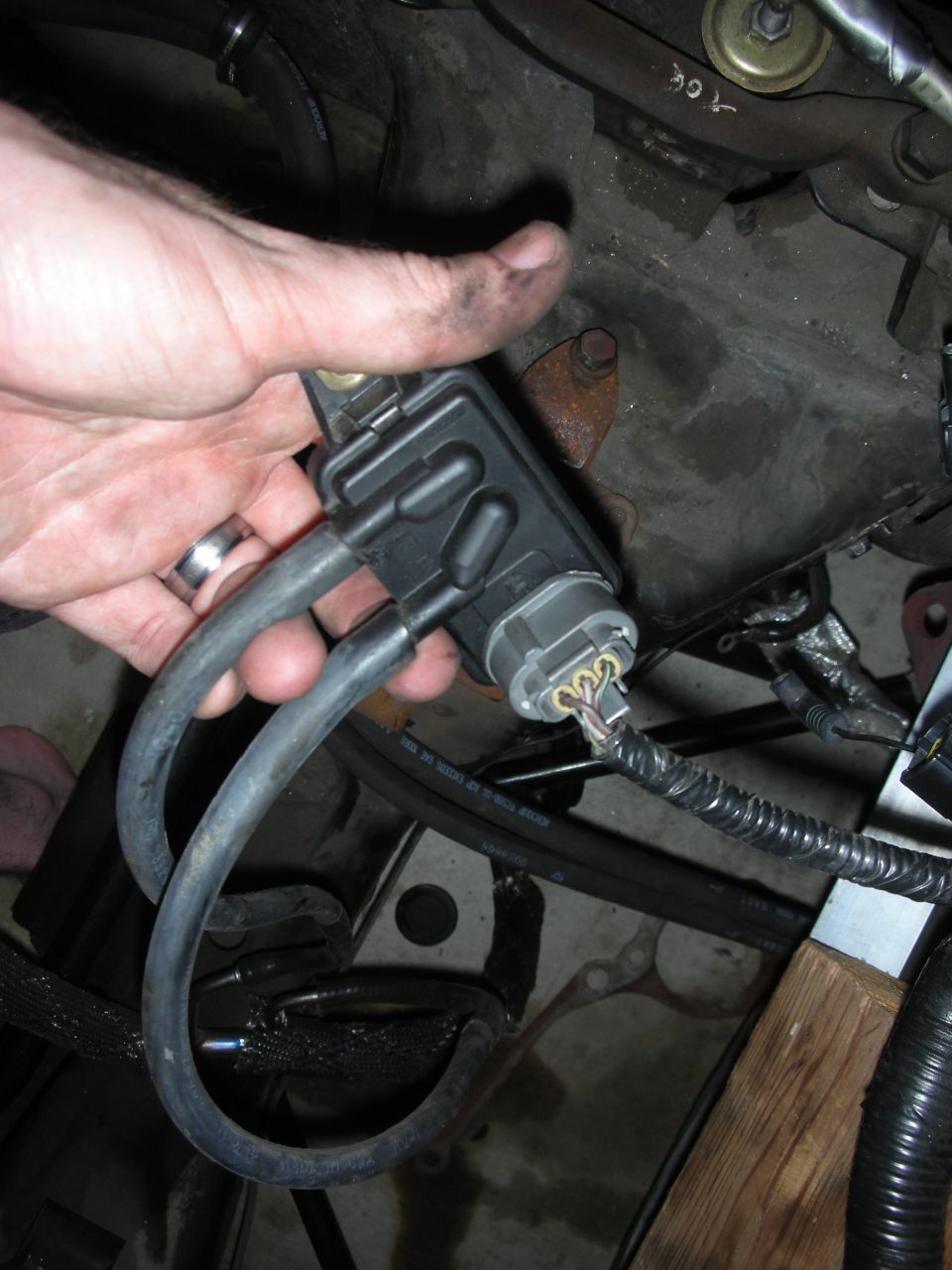 Hand holding a black plastic car part with two rubber hoses and a gray electrical connector