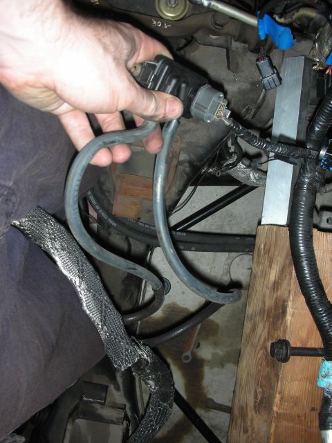 1992 Ford Crown Victoria - A hand disconnects a wiring harness and hoses from an engine component, showing a complex network of wires and tubes.