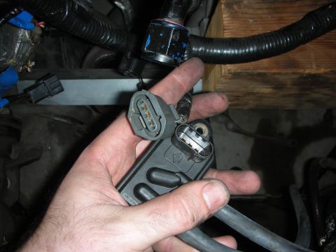 1992 Ford Crown Victoria - A hand holds a black engine sensor with two electrical connectors, disconnected from the engine.