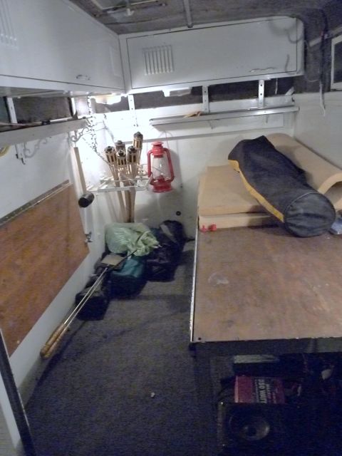 2006 Ford E350 - Interior of a camper conversion mid-build, with white-painted walls and overhead cabinets, gray carpeted floor, and a bare plywood bed plat…