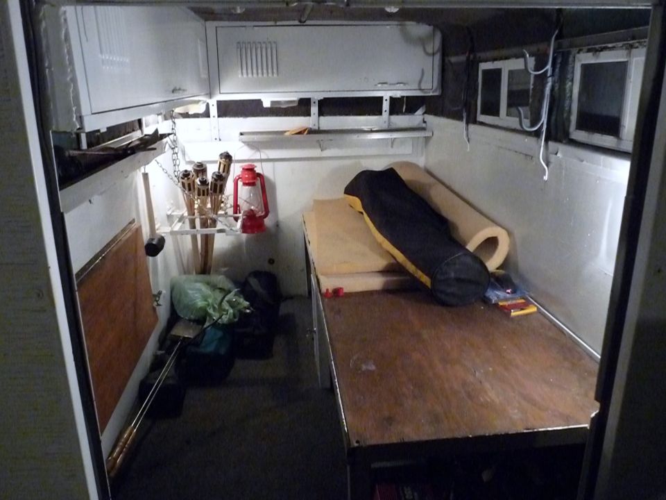 Interior of a cargo van with a wooden platform, sleeping bag, and torches