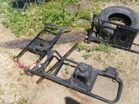 1991 Ford Bronco - Disassembled vehicle frame components and a spare tire are scattered on the ground outdoors.