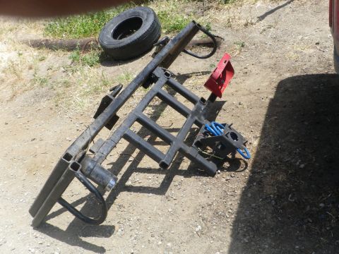 1991 Ford Bronco - A spare tire and a black trailer hitch rack with a red bracket are shown on the ground.