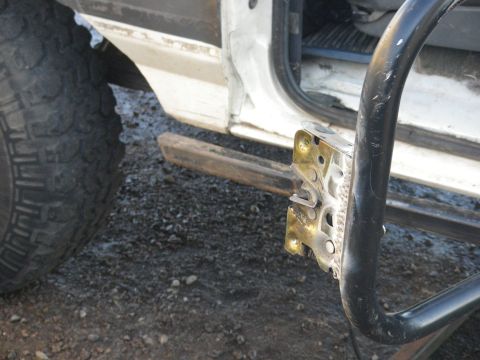 1991 Ford Bronco - Close-up of a white vehicle's door latch mechanism and a portion of its tire.