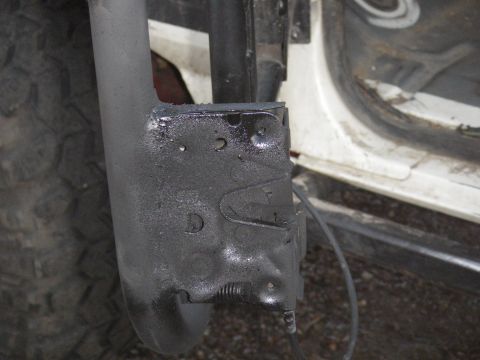 1991 Ford Bronco - Detail of a vehicle's frame and tire, showing a black painted metal bracket.