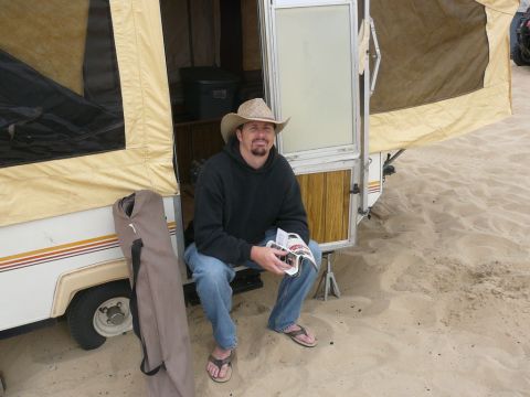 1988 Ford Bronco - A man relaxes in his pop-up camper, parked on a sandy beach, holding a magazine.