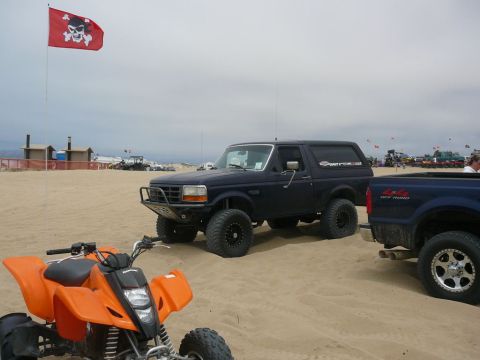 1988 Ford Bronco - Ford Bronco and ATV on a sandy beach with a pirate flag flying.
