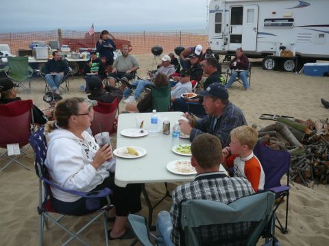 1988 Ford Bronco - A group enjoys a meal on the beach next to a large RV and a campfire.