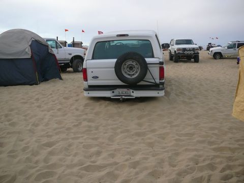 1988 Ford Bronco - White 1988 Ford Bronco on a beach with multiple vehicles and camping tents.