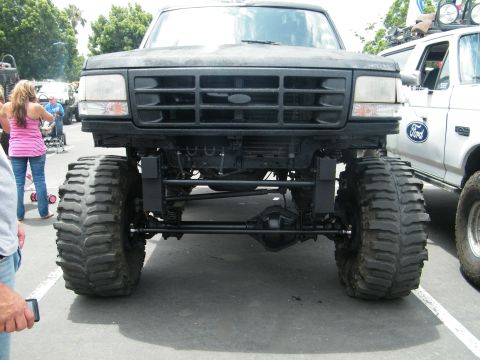 1982 Ford Bronco - This heavily modified black Ford truck features oversized tires and a lifted suspension, seen from a front-facing perspective.