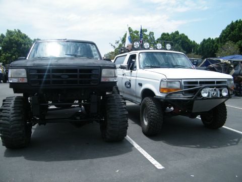 1982 Ford Bronco - Two heavily modified Ford trucks, a black one and a white one, are parked facing forward.