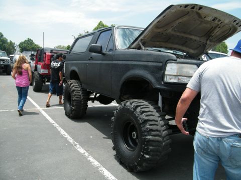 1982 Ford Bronco - A heavily modified black Ford Bronco is parked in a lot, its hood up, alongside other vehicles.