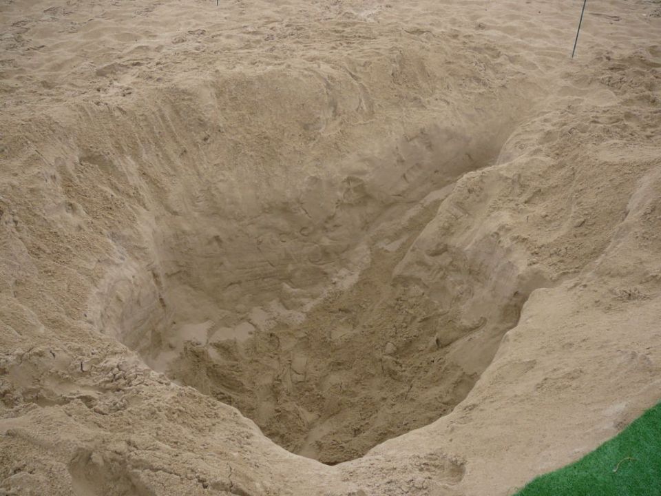 Large sand pit with steep, uneven walls and a thin pole in the background
