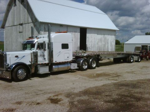 1979 Ford Bronco - A white semi-truck with a flatbed trailer is parked in front of a large barn, with another vehicle visible in the background.