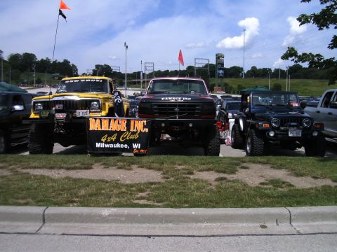 1994 Ford F-250 - Three lifted off-road vehicles are displayed with a club banner, under a partly cloudy sky.