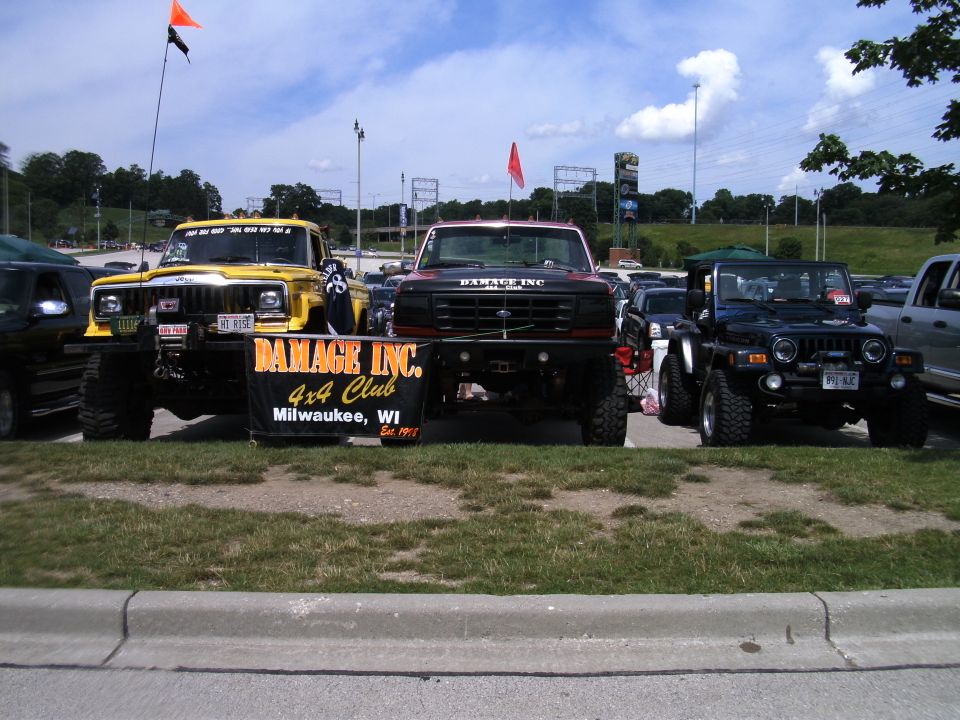 Yellow Jeep Cherokee, black Ford F-250, and blue Jeep Wrangler parked together with a 'Damage Inc. 4x4 Club' banner