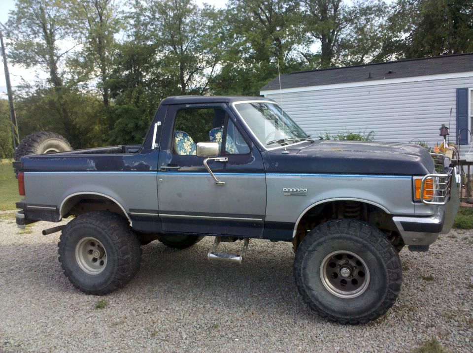 Blue and silver lifted Ford Bronco, side view, with spare tire on back