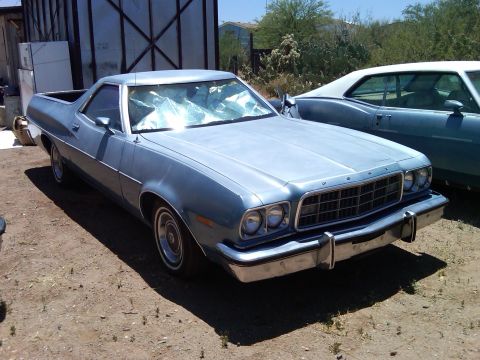 1973 Ford Ranchero - Light blue 1973 Ford Ranchero with a cracked windshield sits in a dusty lot next to another vehicle.