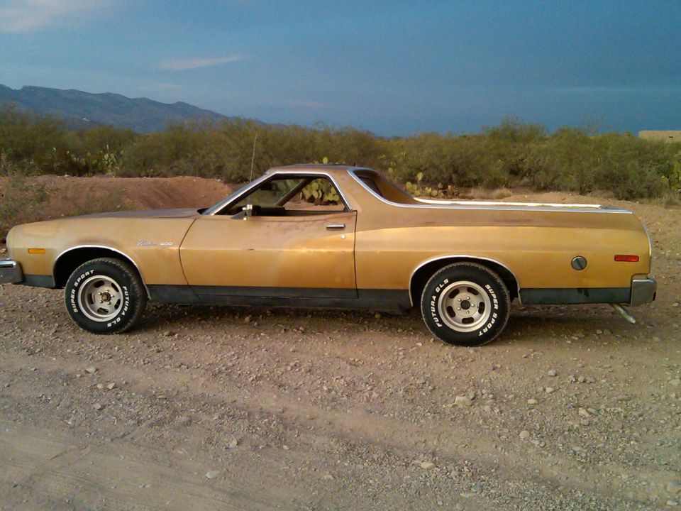 Gold Ford Ranchero parked on a dirt road with desert brush and mountains in the background