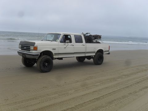 1991 Ford F-350 - A lifted white Ford F-350 crew cab truck sits on the sand with the ocean in the background.