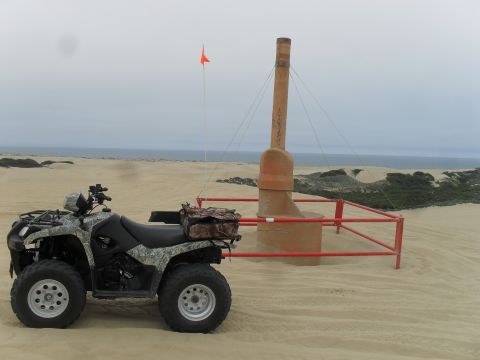 1991 Ford F-350 - An all-terrain vehicle is parked on a sandy landscape near a distinctive monument and the ocean.