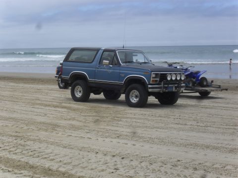 1991 Ford F-350 - This blue SUV with a black top is parked on a sandy beach, with a trailer carrying a blue ATV behind it.