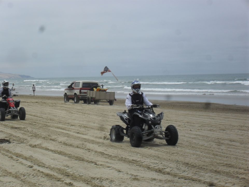 ATVs and a pickup truck with a trailer on a sandy beach near the ocean