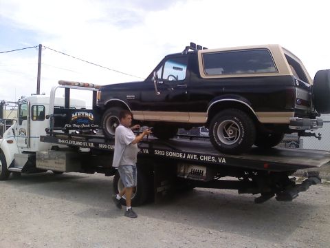 1990 Ford Bronco - A black and tan 1990 Ford Bronco is loaded onto a tow truck.