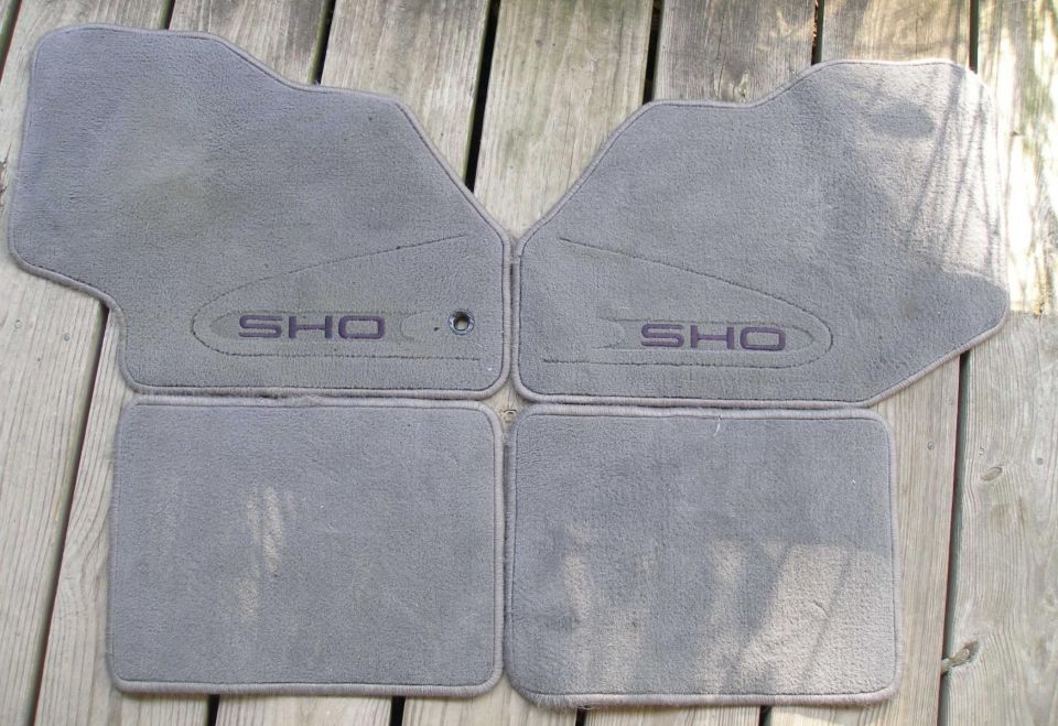 Four gray car floor mats with "SHO" embroidered on two of them