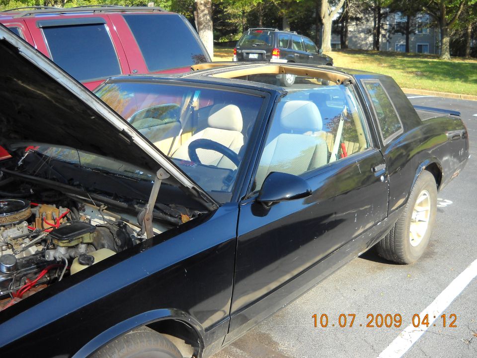 Black coupe with open hood, tan interior, and sunroof, parked next to a red SUV