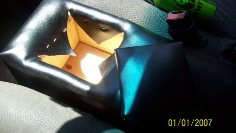 2004 Ford Crown Victoria - Close-up of a damaged black vinyl car interior part, revealing exposed wooden structure.