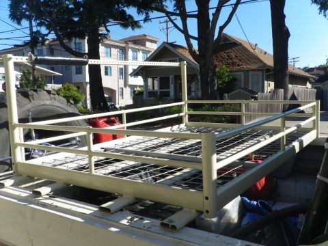 1991 Ford Bronco - A truck bed rack holds two red jerry cans and a blue tarp, with houses in the background.
