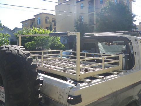 1991 Ford Bronco - A pickup truck bed is fitted with a custom cargo rack and a large spare tire is mounted on the side. The Supermotors.net logo is visible in…