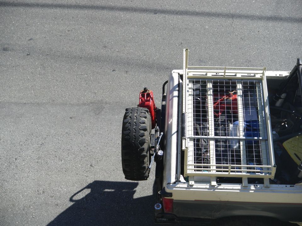 Spare tire and red jerry can mounted on the rear of a pickup truck with a cargo cage in the bed