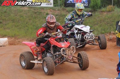 2004 Honda TRX 400 EX - Two riders compete in an ATV race on a dusty track, with spectators and banners in the background.