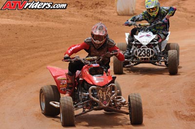2004 Honda TRX 400 EX - Two ATVs compete on a dusty track, with one rider in red and the other in camouflage gear.