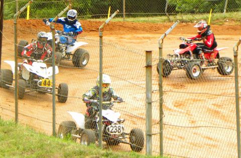 2004 Honda TRX 400 EX - ATVs compete on a dirt track, with riders in full gear. A fence partially obstructs the view of the race.
