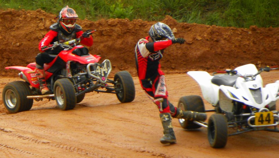 Red ATV with rider in front, white ATV with rider in middle on dirt track. Number 44 visible on white ATV