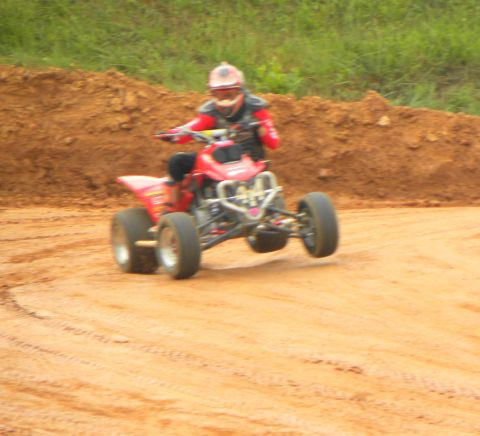 2004 Honda TRX 400 EX - A rider on a red ATV navigates a dirt track, with one front wheel lifted off the ground.