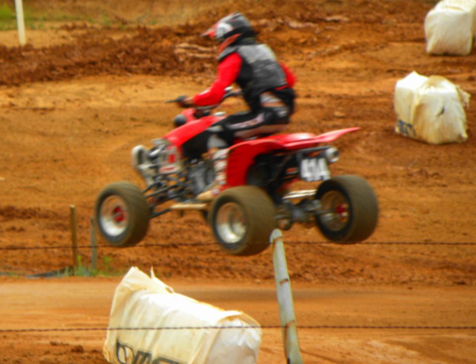 Red ATV with rider in helmet and red jacket mid-air on a dirt track. Number 414 visible on rear fender