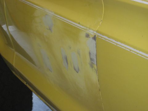 1978 Ford Bronco - A close-up view of a yellow vehicle's body panel shows areas of body filler and a white stripe, indicating repair work.
