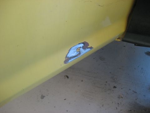 1978 Ford Bronco - A close-up view of a damaged section on a yellow vehicle's side panel shows rust and repair work.