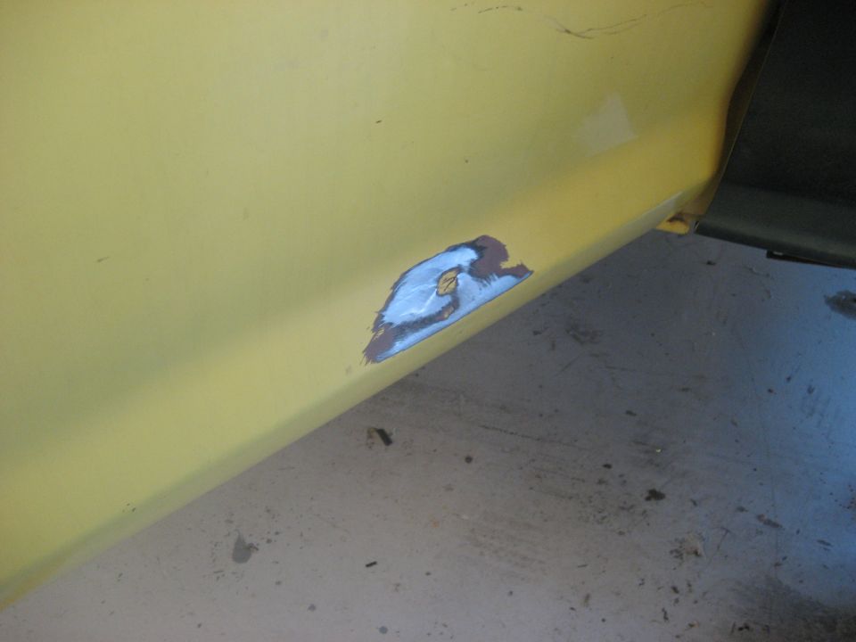 Yellow vehicle side panel with a patch of exposed metal, primer, and blue paint